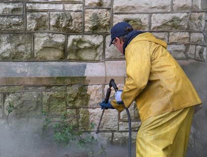 Technician steam cleaning a stone facade